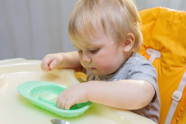 istock Little child sits on a high chair and eats with a spoon 1310759467