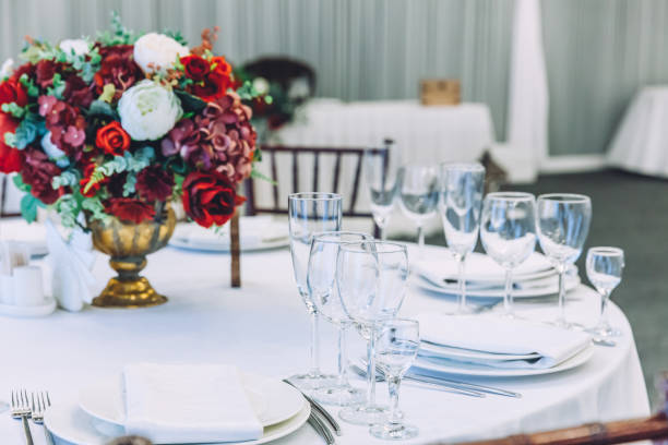 istock Fancy table set for dinner with flower composition in restaurant, luxury interior background. Wedding elegant banquet decoration and items for food arranged by catering service on white table 1310763957