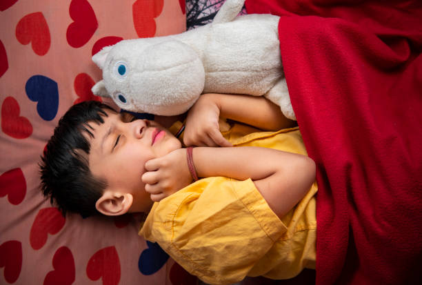 Adorable little boy sleeping in bed with his toys at home, High angle view, Night shot