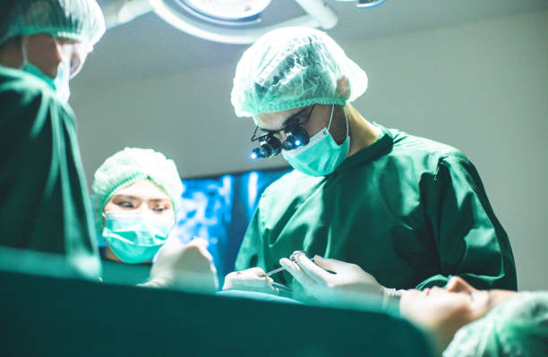外科医の医師は手術室で手術前に外科用手袋を着用しています。アジアの医師と外科静脈のための手術室の助手。 - 美容整形医 ストックフォトと画像