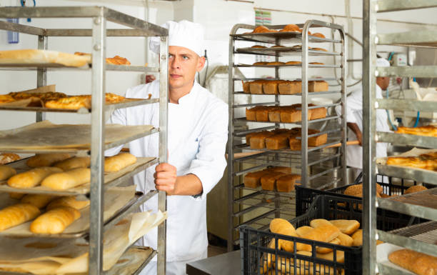 istock Male baker carrying rack trolley with bread 1310774430