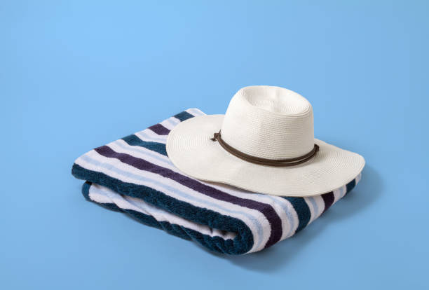 Large white brim hat on a striped beach towel with a light blue background Large white brim hat on a striped beach towel with a light blue background beach towels bulk stock pictures, royalty-free photos & images