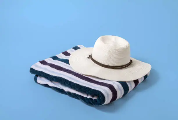 Photo of Large white brim hat on a striped beach towel with a light blue background