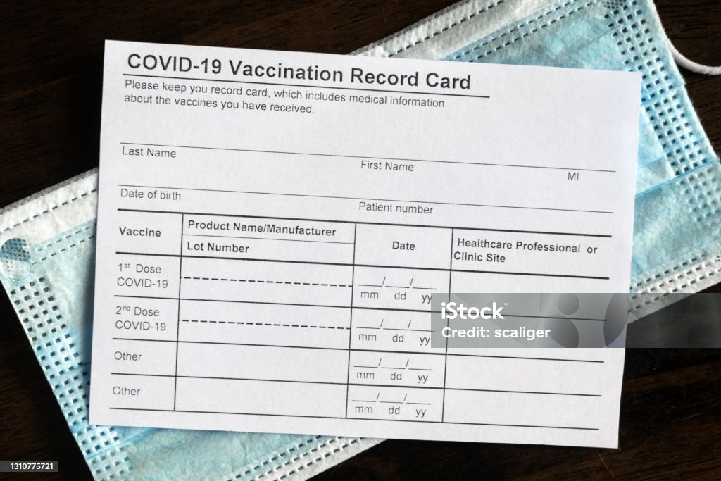 COVID-19 Vaccination Record Card on desk COVID-19 Vaccination Record Card on desk, coronavirus immunization certificate and surgical mask. Top view of paper medical form required for travel. Concept of corona virus vaccine, safety, tourism. Immunization Certificate Stock Photo