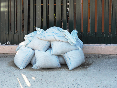 White sandbags piled in a pile lie on the street near the fence