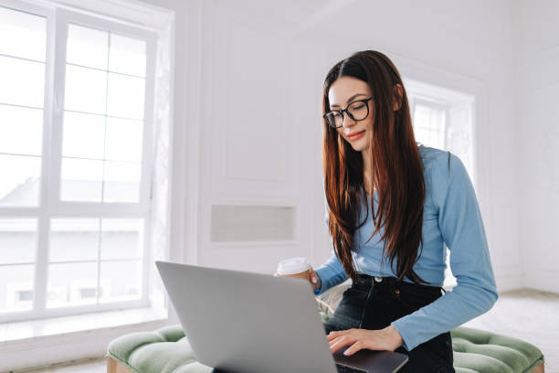 istock Attractive pretty young woman in eyeglasses freelancer using laptop computer at home, typing text and drinking coffee. 1310783164