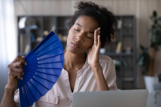 Unwell biracial woman wave with hand fan working on computer