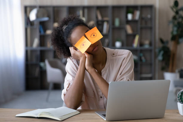 Exhausted biracial woman feel sleepy at home office Exhausted young African American woman work on computer at home office, have sticker pads on eyes feel sleepy. Tired millennial biracial female employee student suffer from exhaustion or fatigue. wasting time stock pictures, royalty-free photos & images