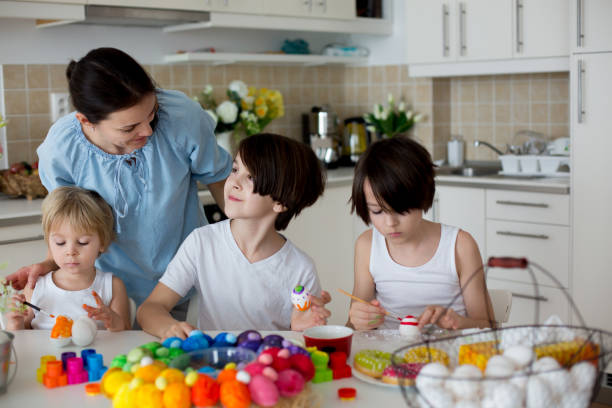 istock Three children, sibling brothers, painting easter eggs for decoration, mom helping them 1310788224