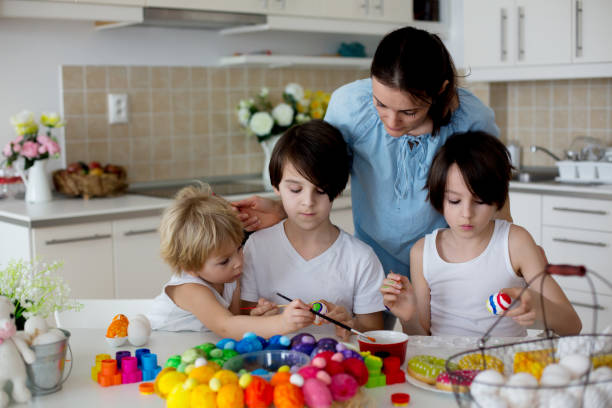 istock Three children, sibling brothers, painting easter eggs for decoration, mom helping them 1310788235