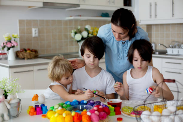 трое детей, братья и сестры, живопись пасхальные яйца для украшения, мама помогает им - face paint child paint rabbit стоковые фото и изображения