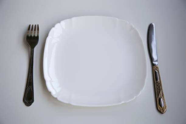 istock Table setting with a clean white plate, fork and knife laid out on a white background 1310792305