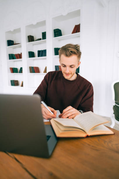 istock Young caucasian man college student studying with laptop distantly preparing for test exam writing essay doing homework at home or college library. 1310792480