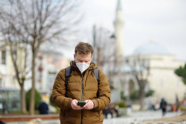 dojrzały mężczyzna w masce za pomocą telefonu na ulicy w stambule, turcja. w słoneczny wiosenny dzień. turysta poruszał się ze swoim smartfonem. - 11817 zdjęcia i obrazy z banku zdjęć