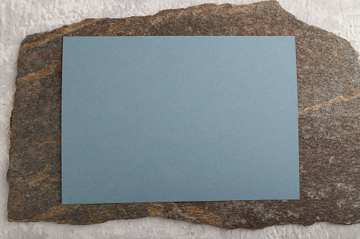 Blue paper business card, mockup with natural stone on gray concrete background. Blank, flat lay, top view, still life, copy space.