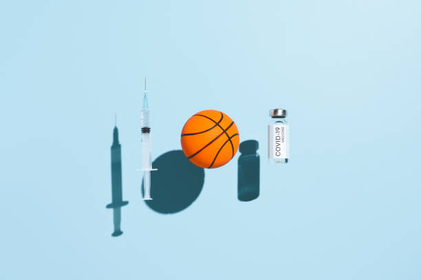 Coronavirus vaccination concept. Vial vaccine, medical syringe, and basketball ball in form virus, levitating over pastel blue background. Top view stock photo