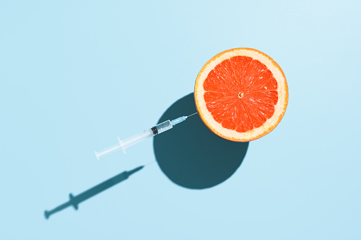 Coronavirus vaccination creative concept. Half grapefruit and a syringe with a vaccine against COVID-19, levitating over pastel blue background. Minimalistic image, top view