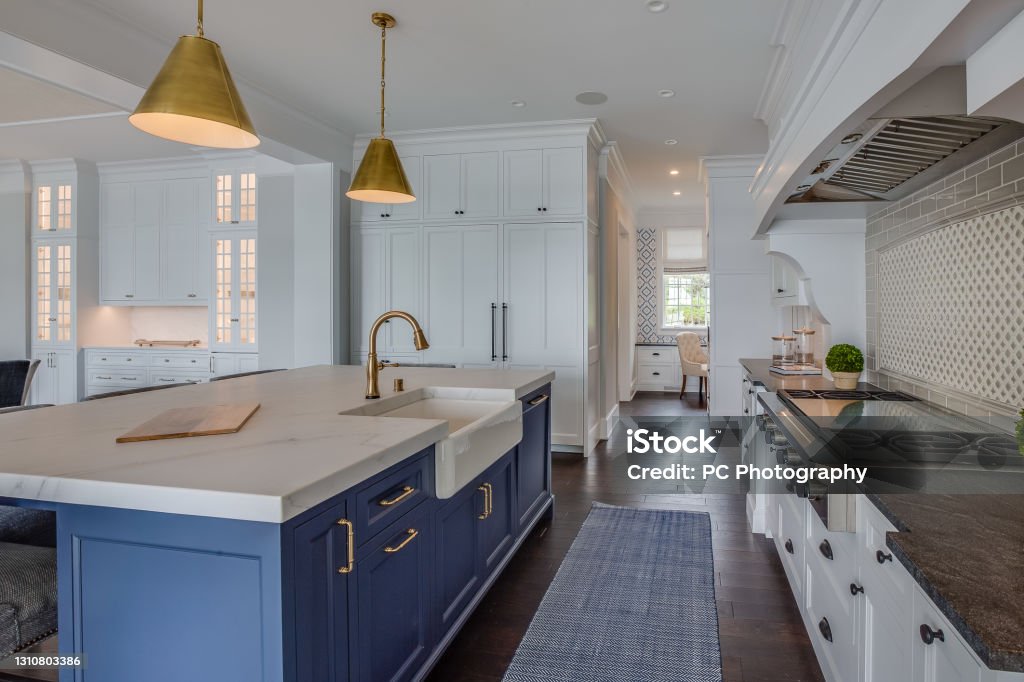 Blue island with brass or brushed gold pendant lights Kitchen galley with dark hardwood floors and blue rug to match island cabinets Kitchen Stock Photo