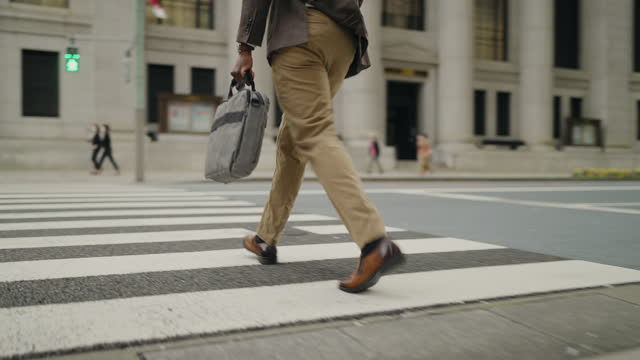 A rear view video of a businessman crossing the street in a financial district in the city.