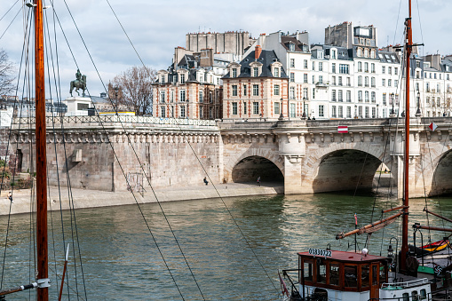 Panorama of Seine quayside, in Paris - Boat in foreground, Pont Neuf and tenement facade in background. Paris, France. March 21, 2021