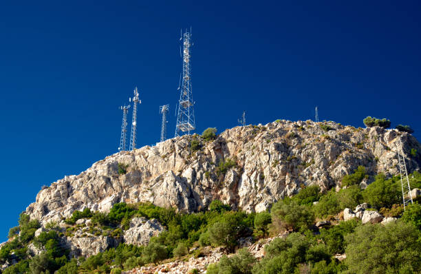 Antennas at rocky mountain peak, sunlight, blue sky, green trees