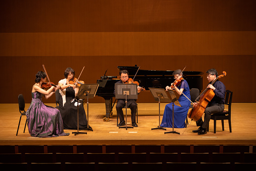 Japanese adult musicians playing violin, viola, cello, and piano, and singing songs at classical music concert.