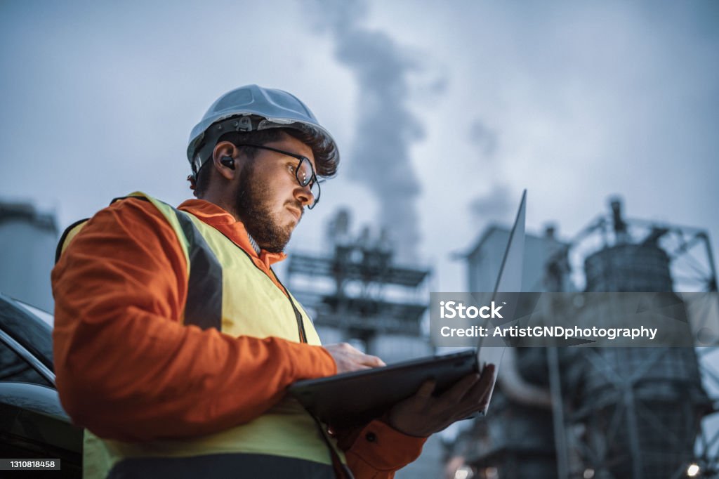 Seriös stilig ingenjör som använder en bärbar dator medan han arbetar inom olje- och gasindustrin. - Royaltyfri Industri Bildbanksbilder