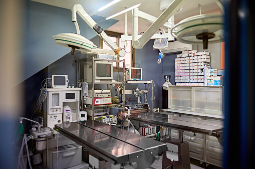 View through doorway of unoccupied room with operating tables, lights, and medical technical equipment.