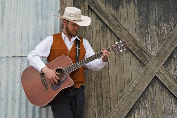 istock Cowboy Plays Guitar by Rustic Barn Door, Copy Space 1310829467