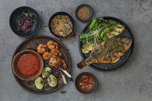 Thai shrimp satay with sweet chili sauce. Barbecued sea bream wild grilled vegetables. Close-up composition on concrete background.