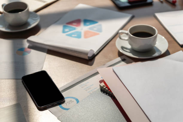 istock Business and work concept. Closeup of smartphone on woking desk with document, chart, notebook, and cup of hot black coffee. 1310843527