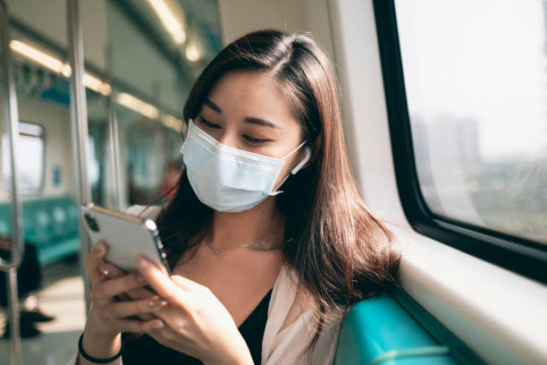 mulher asiática usa máscara, usa smartphone e fones de ouvido e mantém distanciamento social ao se deslocar no metrô ou trem - human lung audio - fotografias e filmes do acervo