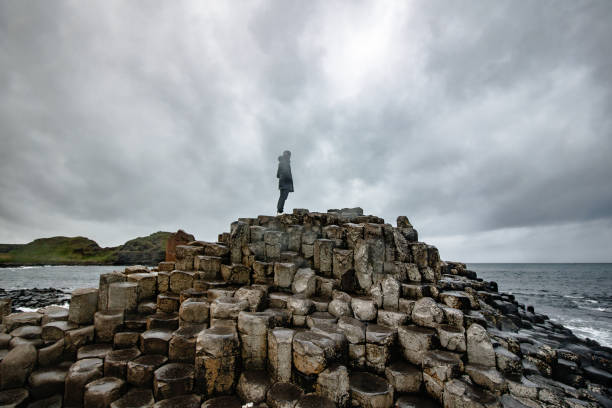 Man watching the horizon and the columnar basaltic in a cloudy day Man watching the horizon and the columnar basaltic in a cloudy day. The picture was taken in the giant's causeway from Northen Ireland giants causeway stock pictures, royalty-free photos & images