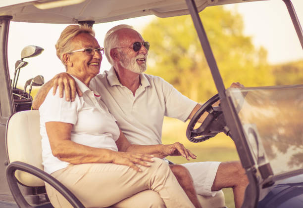 o casal de golfistas felizes está andando em um carrinho de golfe e conversando. - senior couple golf retirement action - fotografias e filmes do acervo