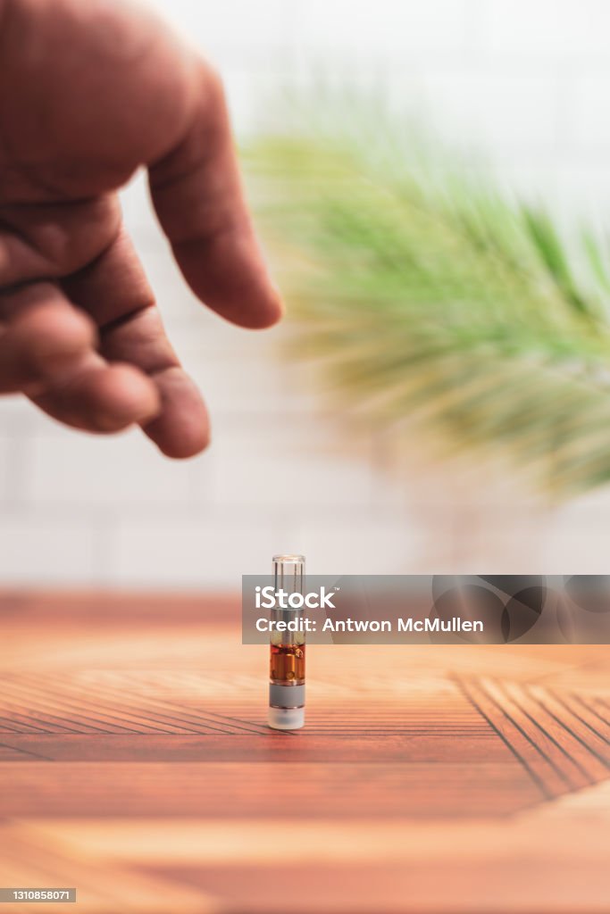 A hand reaches to pick up a cannabis vaporizer cartridge. A hand reaches to pick up a cannabis vaporizer cartridge from a counter at home. Electronic Cigarette Stock Photo