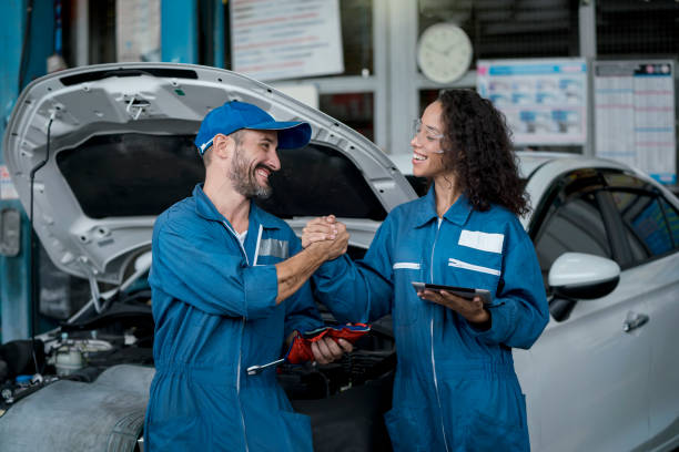 petite entreprise. deux mécaniciens heureux d’automobile dans des uniformes travaillant dans le service automatique avec la voiture. deux mécaniciens de poignée de main d’hommes dans le service de réparation automatique. - auto repair shop customer auto mechanic mechanic photos et images de collection