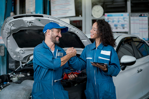 Smallbusiness. Two happy auto mechanics in uniforms working in auto service with car. Two men handshake mechanics in auto repair service.