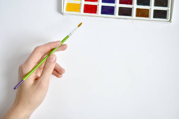 A hand with a brush reaches for watercolors. Mockup for artwork. Painting with paints