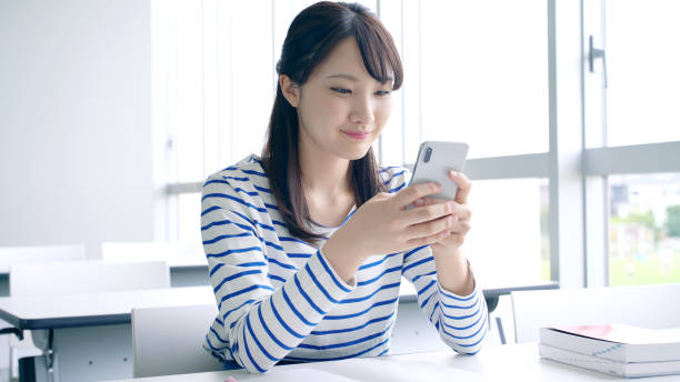 スマートフォンを使ったアジアの若手女子学生。 - 女子大生 ストックフォトと画像