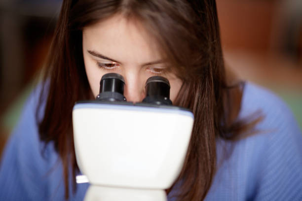 istock Close-up on female high school student looking through microscope binoculars 1310864411