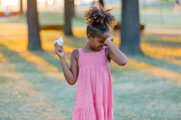 Cute African-American Girl is Having an Allergy Outside and Rubbing her Eyes. Young African Girl is Walking in the Park But Feeling Uncomfortable Due to the Problems with her Eyes, so She is Rubbing them. human eye scratching allergy rubbing stock pictures, royalty-free photos & images
