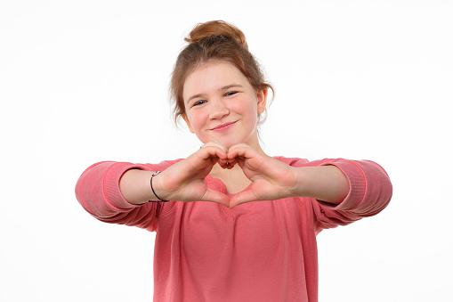 Love you. Young pretty teen girl wearing in pink casual sweatshirt, smiling happily, making heart symbol by hands. Romantic concept. Studio shot, white background