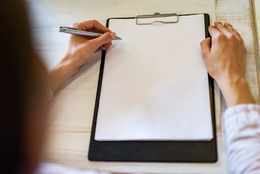 Close up of unrecognizable businesswoman writing on a paper in the office. Copy space.