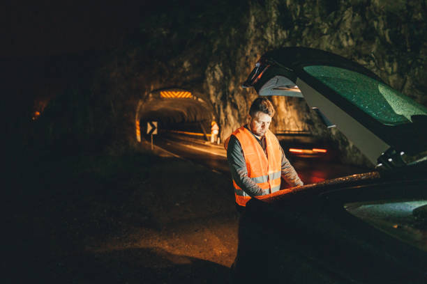 istock Driver with reflective waistcoat looking at car trunk on roadside 1310868588