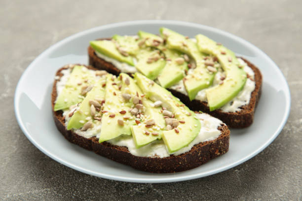 istock Avocado sandwich on dark rye bread made with fresh sliced avocados on grey background. 1310869874