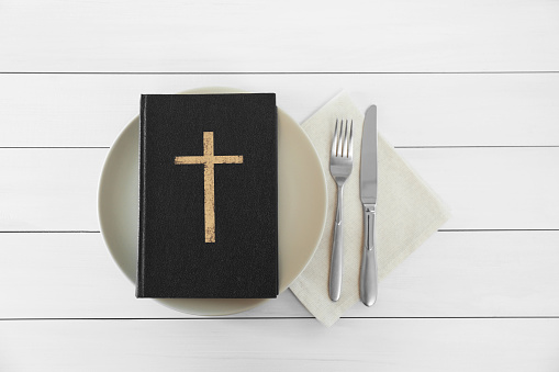 Plate with Bible and cutlery on white wooden table, flat lay. Lent season