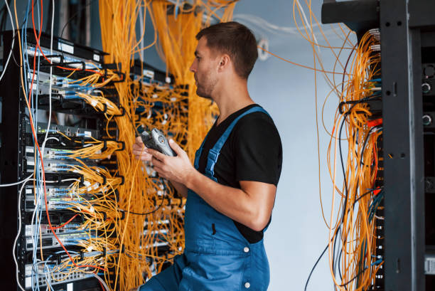 istock Young man in uniform with measuring device works with internet equipment and wires in server room 1310873033