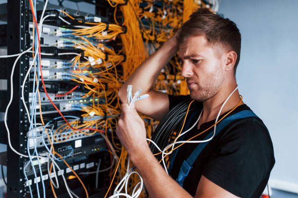 istock Young man in uniform feels confused and looking for a solution with internet equipment and wires in server room 1310873717