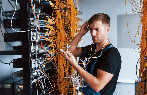 istock Young man in uniform feels confused and looking for a solution with internet equipment and wires in server room 1310873730