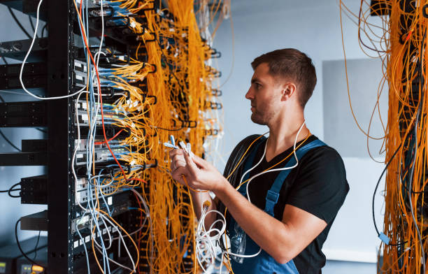 istock Young man in uniform feels confused and looking for a solution with internet equipment and wires in server room 1310873757